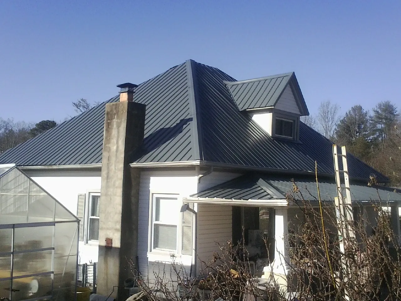 Dark blue standing seam metal roof on a white farmhouse with dormer — Slate & Tile Roof Repair by Roofing Brothers in Monett