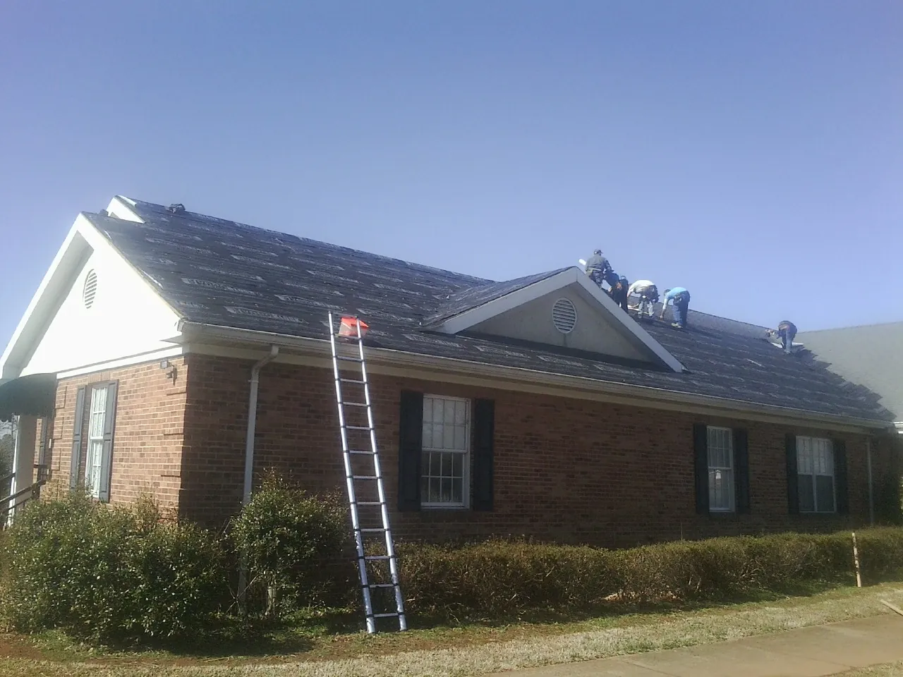 Crew tearing shingles off a brick ranch roof with a ladder set — Metal Roof Repair work by our crew in Monett
