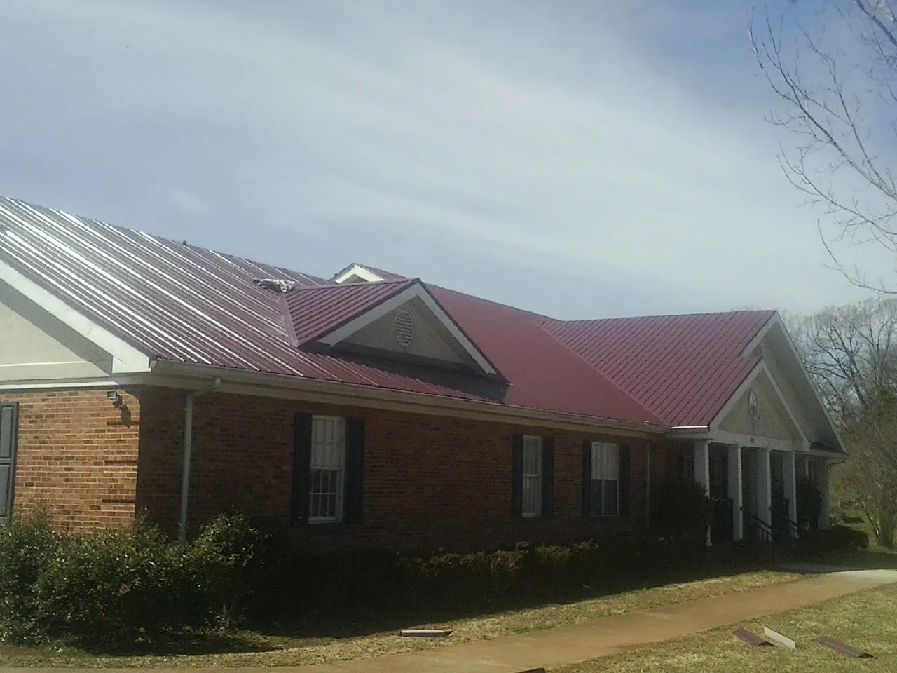 Red metal roof with gabled entries on a long brick building, from a Hail Damage Roof Repair job in Monett
