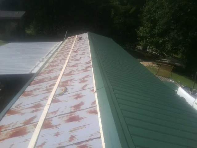 Old rusted panels beside newly installed green metal roofing — Wind Damage Roof Repair by Roofing Brothers in Monett
