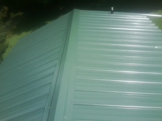 New green metal panels meeting at the ridge of a roof — Flat Roof Repair work by our crew in Monett