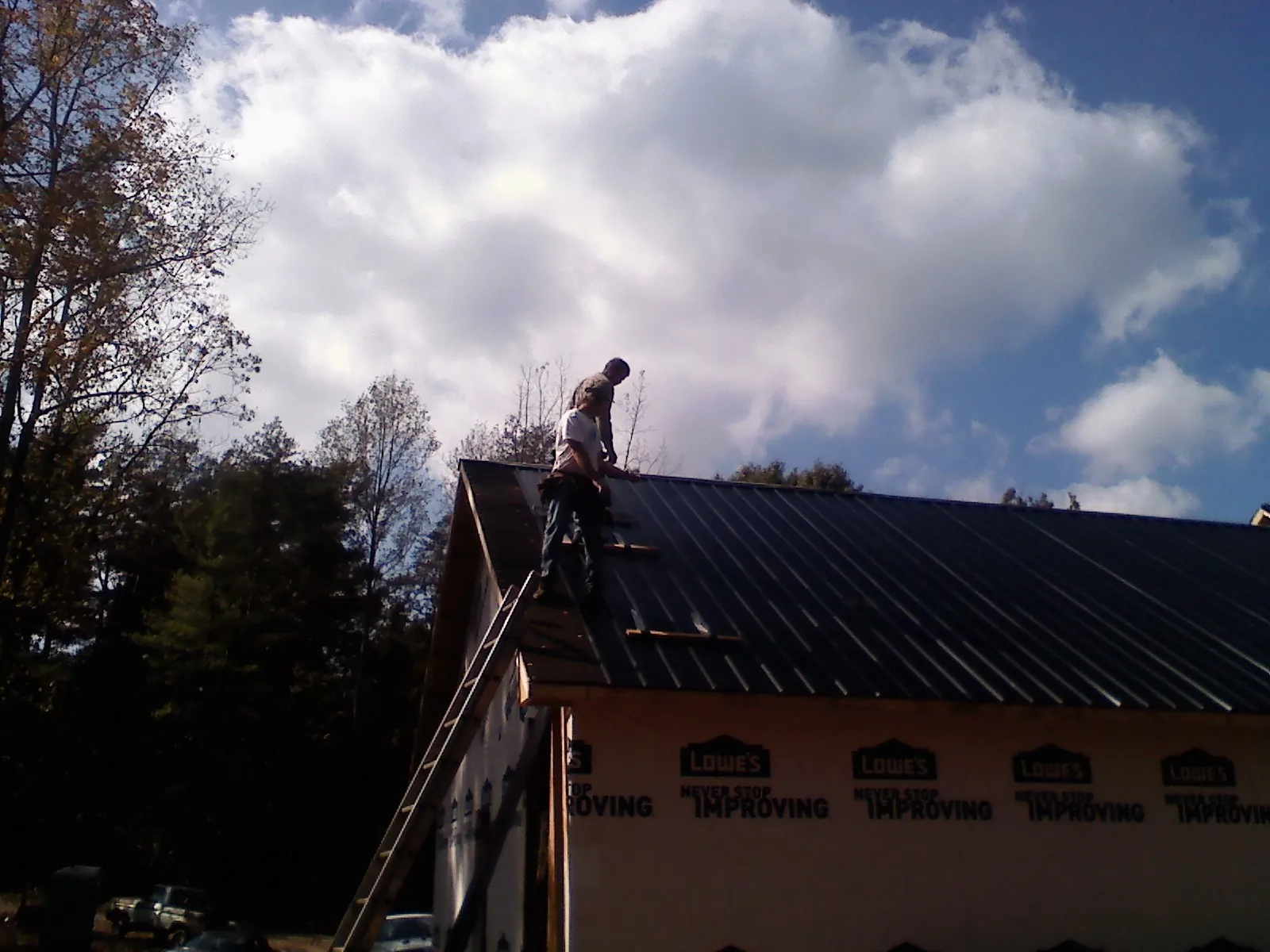 Roofer fastening dark metal panels high against a cloudy sky, from a Roof Inspection job in Monett