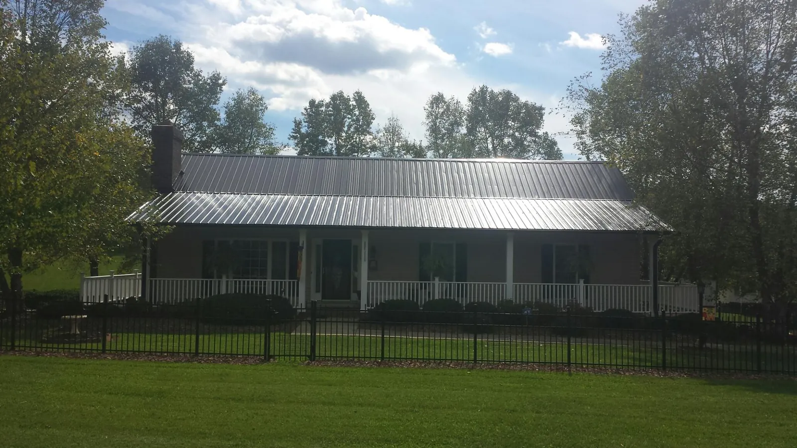 Gray metal roof on a brick ranch with a full width front porch — Gutter Guard Installation work by our crew in Monett