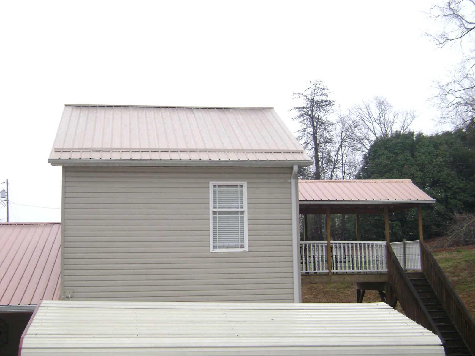 Tan metal roofs on a two story addition and attached porch, from a Roof Replacement job in Monett